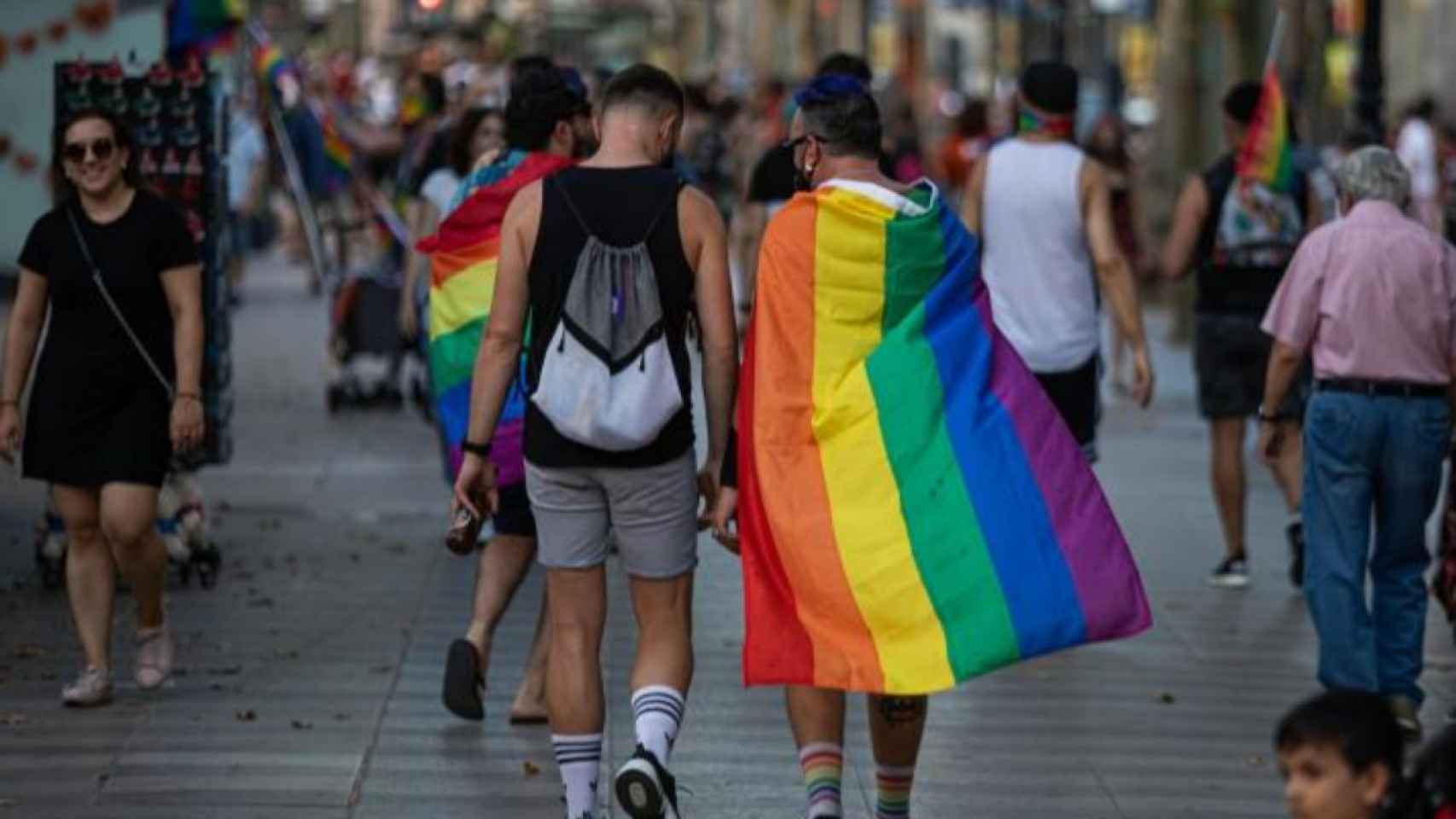Dos personas paseando por Madrid, una de ellas con la bandera LGTB.