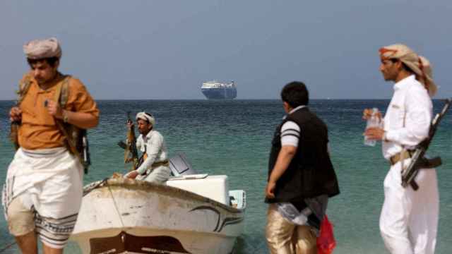 Hombres armados permanecen en la playa mientras el barco comercial Galaxy Leader, capturado por los hutíes de Yemen el mes pasado, está anclado frente a la costa del país de al-Salif el 5 de diciembre.