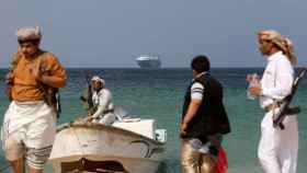Hombres armados permanecen en la playa mientras el barco comercial Galaxy Leader, capturado por los hutíes de Yemen el mes pasado, está anclado frente a la costa del país de al-Salif el 5 de diciembre.