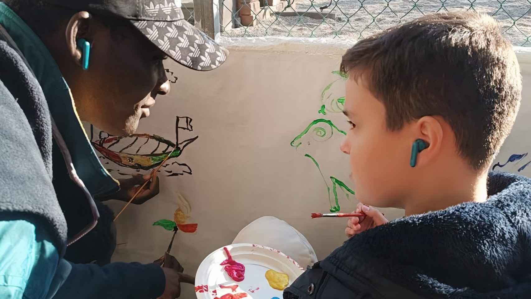 Uno de los migrantes realiza un mural junto a un estudiante del centro.