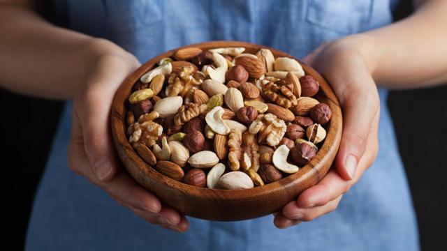 Imagen de las manos de una mujer sosteniendo un bol con nueces, pistachos, almendras y avellanas