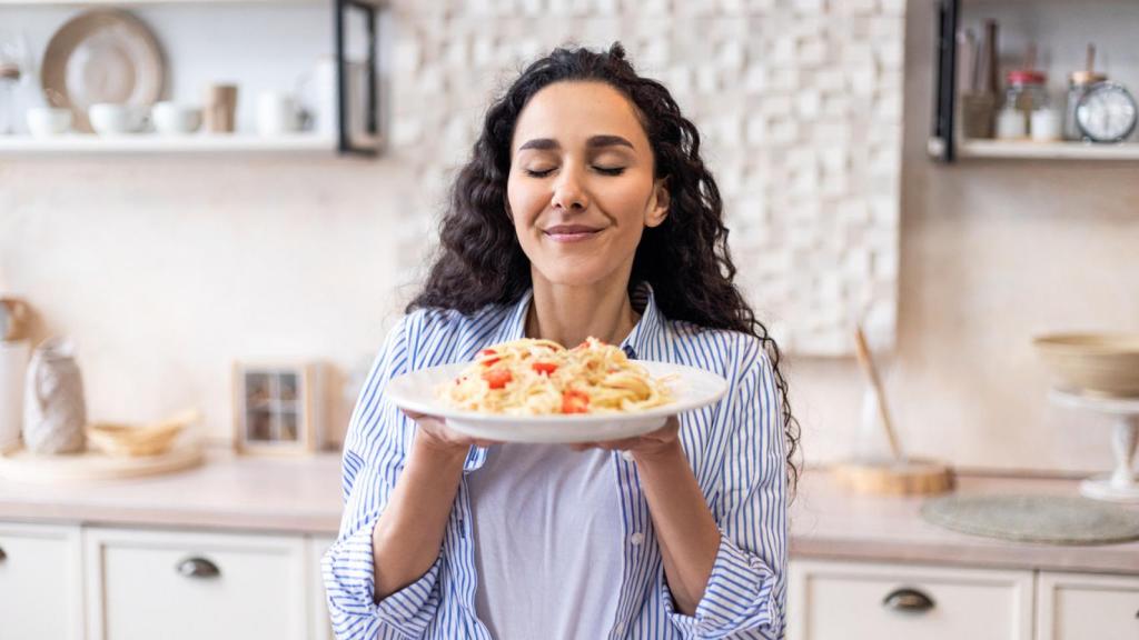 Una mujer, oliendo un plato de pasta.