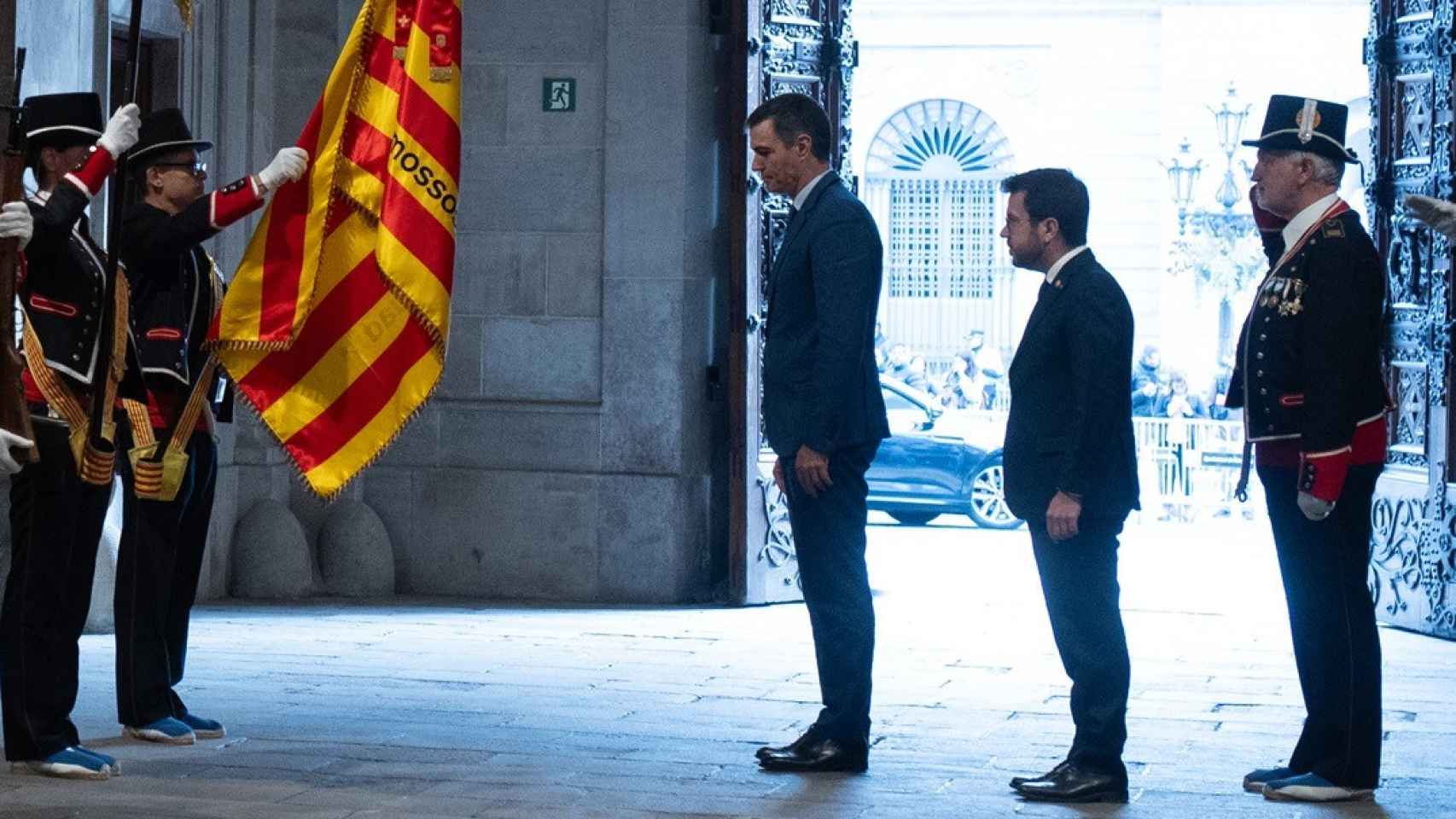 Pedro Sánchez se inclina ante la 'senyera', junto a Pere Aragonès, antes de su reunión en el Palau de la Generalitat.