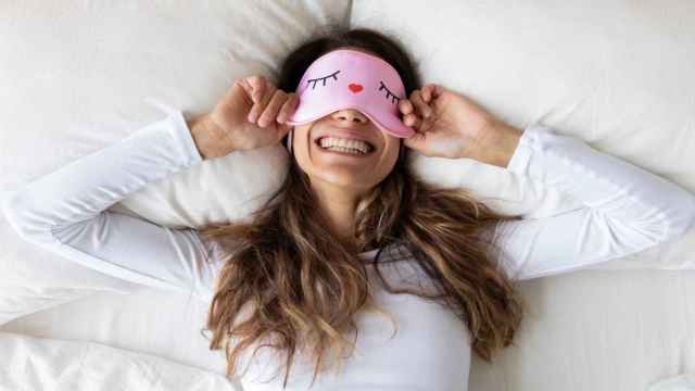 Imagen de una mujer en la cama sonriendo con un antifaz