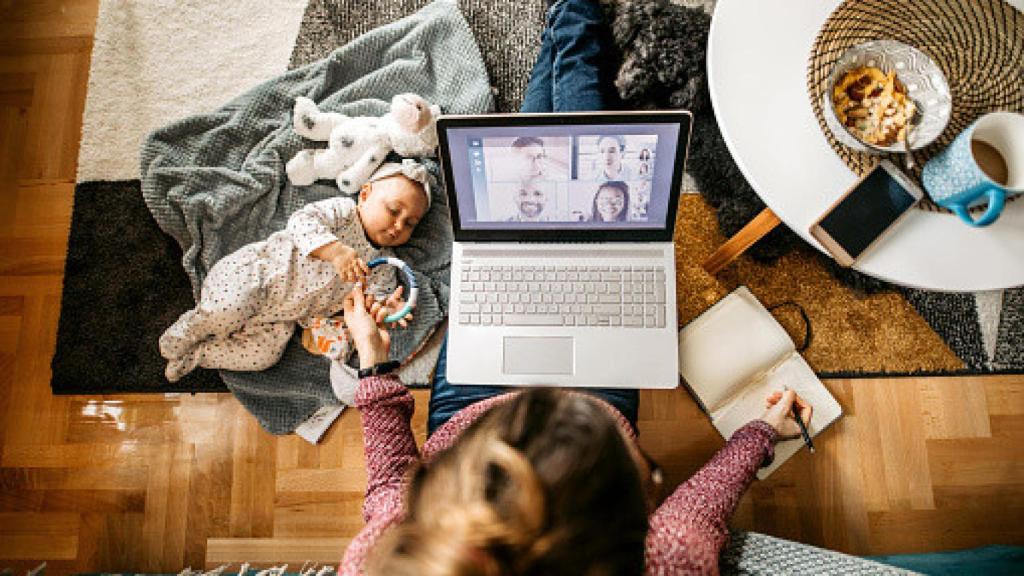 Una mujer teletrabajando junto a su bebe.