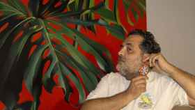 El pintor Manuel León posa con uno de los pendientes que ha confeccionado en su taller delante de un cuadro suyo.