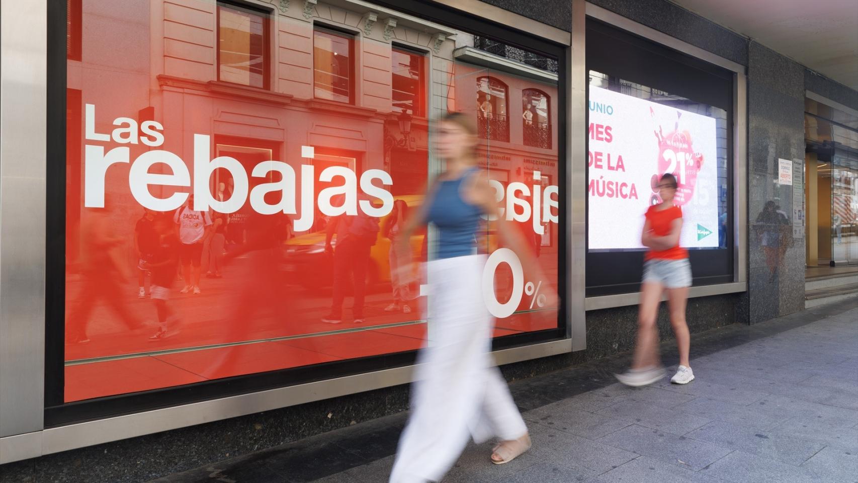 Varias personas pasan al lado de un cartel de rebajas en un escaparate en Madrid.