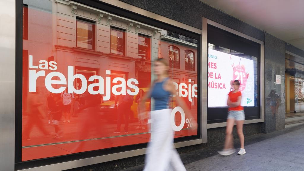 Varias personas pasan al lado de un cartel de rebajas en un escaparate en Madrid.