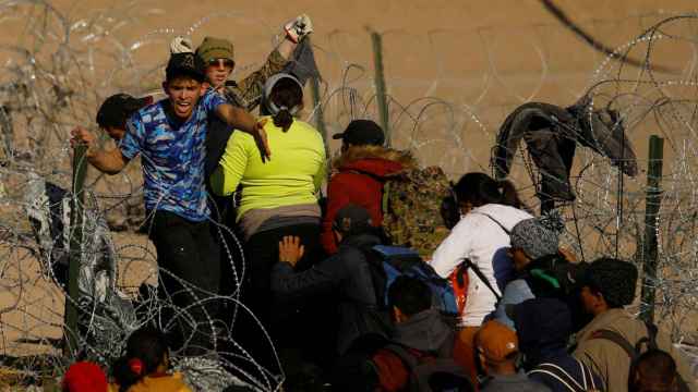 Inmigrantes intentan cruzar una valla de alambre de púas en la frontera de México con Texas.