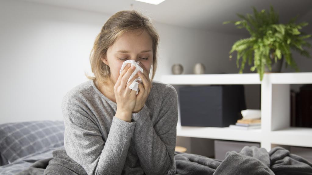 Una mujer enferma sonándose la nariz en la cama.