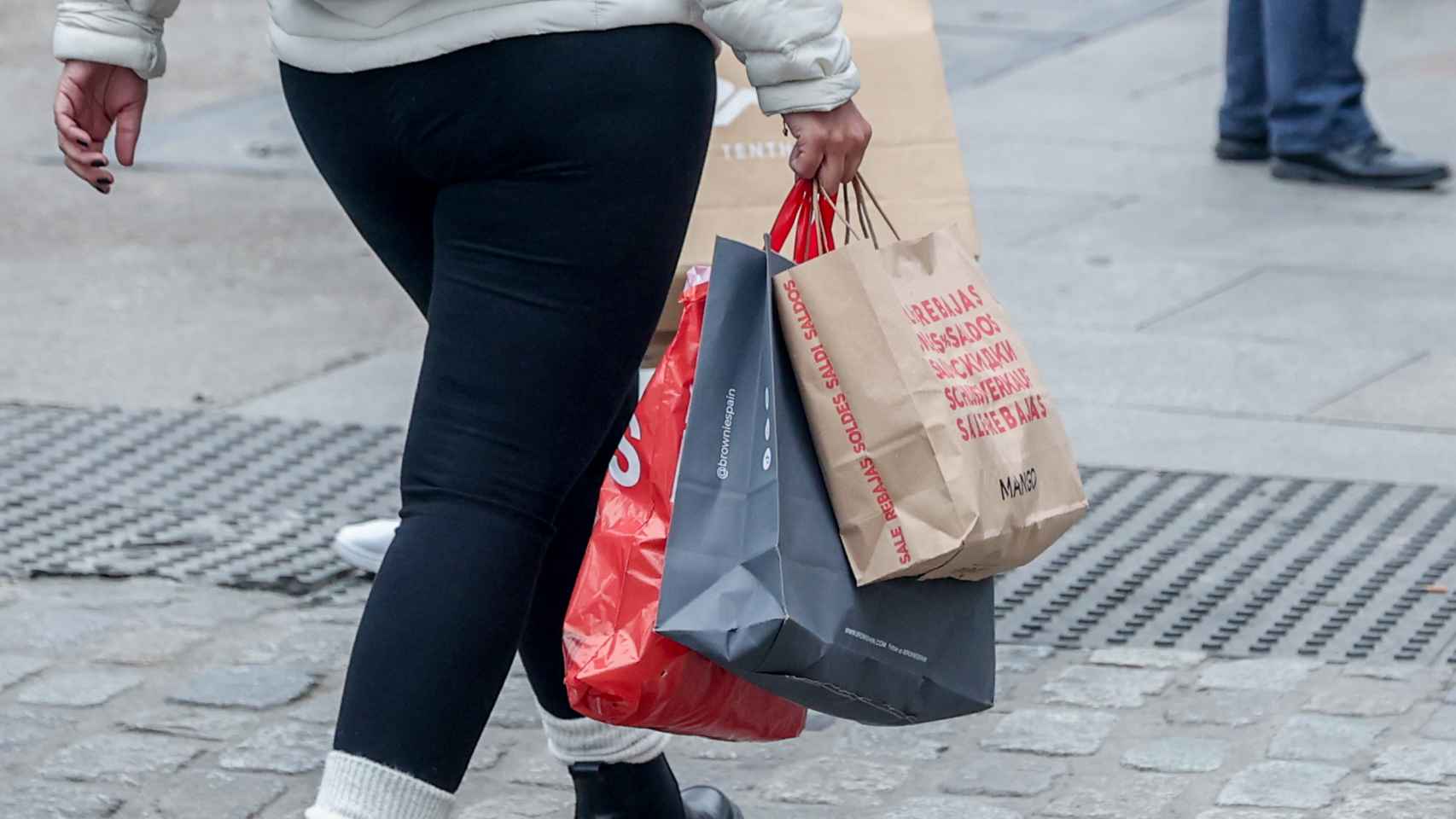 Una persona camina con varias bolsas de compras en la calle comercial de Preciados
