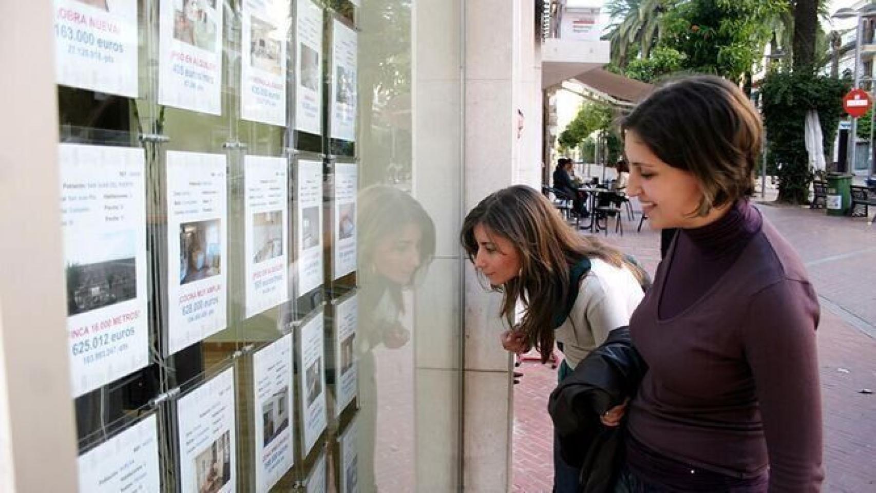Dos jóvenes miran anuncios en una inmobiliaria.