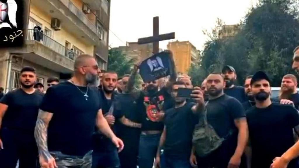 Un grupo de hombres con camisetas negras porta una cruz y un emblema de Junoud al-Rabb.