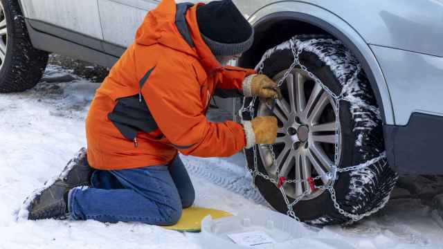 Un hombre colocando cadenas de nieve en un coche.