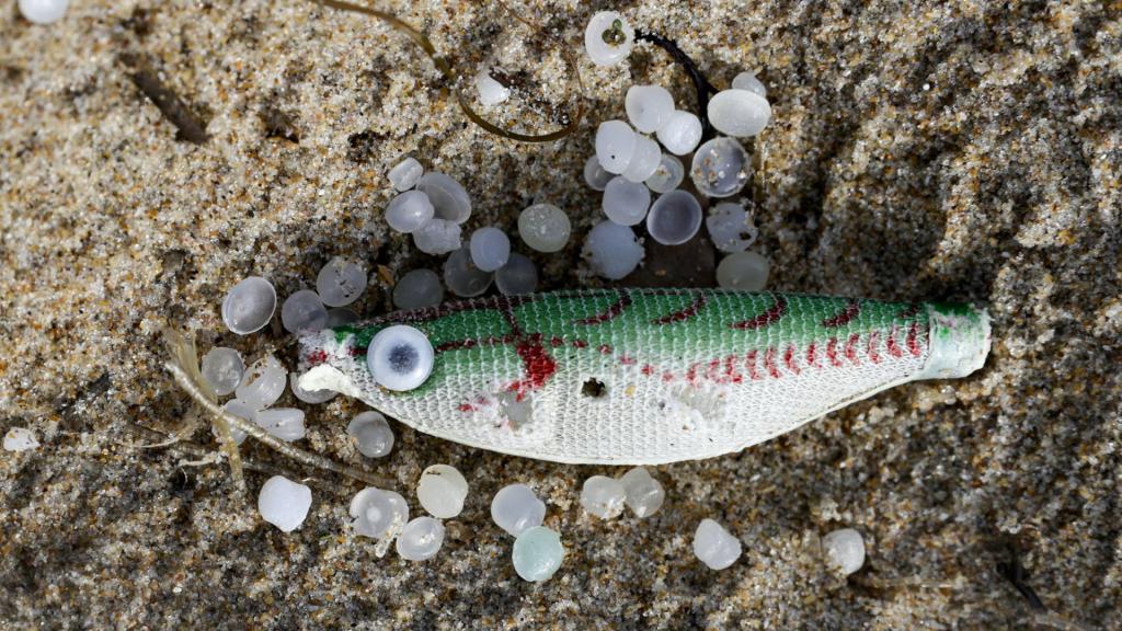 Un pez sintético, empleado como señuelo de pesca, entre varios pellets de plástico.