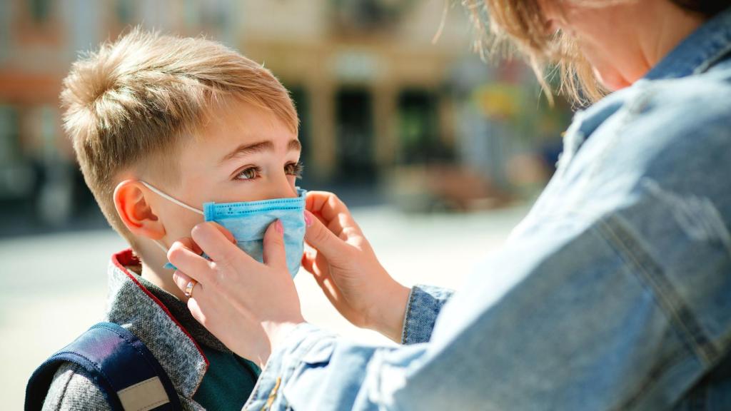 Madre pone una mascarilla a su hijo, en una imagen de Shutterstock.