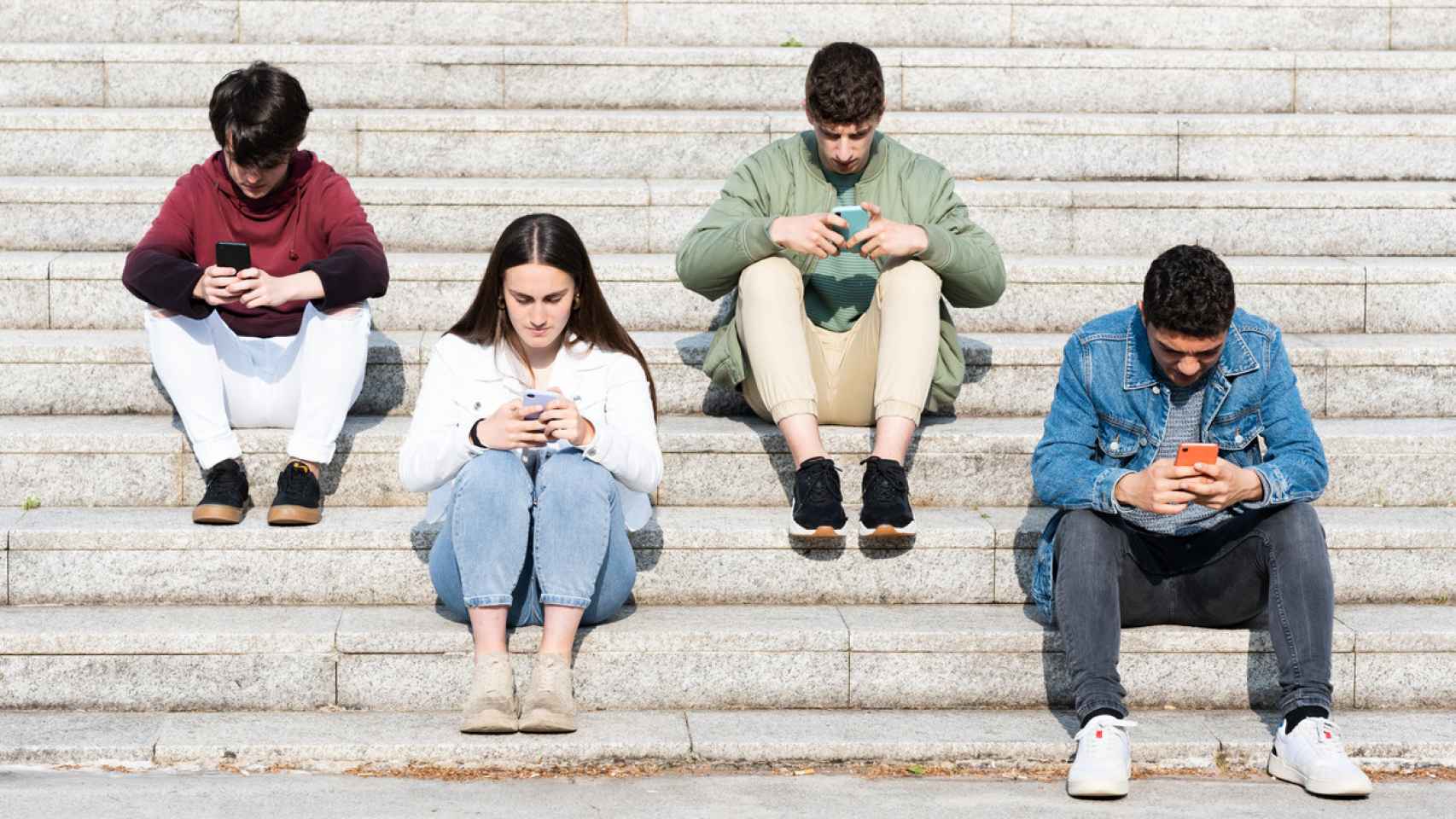 Un grupo de jóvenes utiliza sus teléfonos móviles en unas escaleras.
