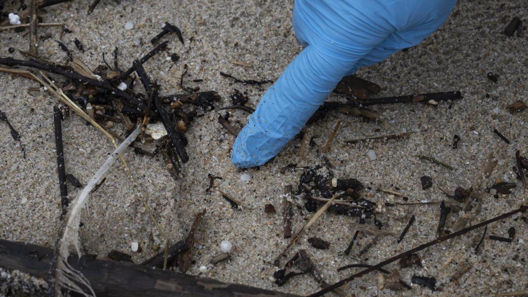 Un voluntario recoge pellets en la playa de Samil.