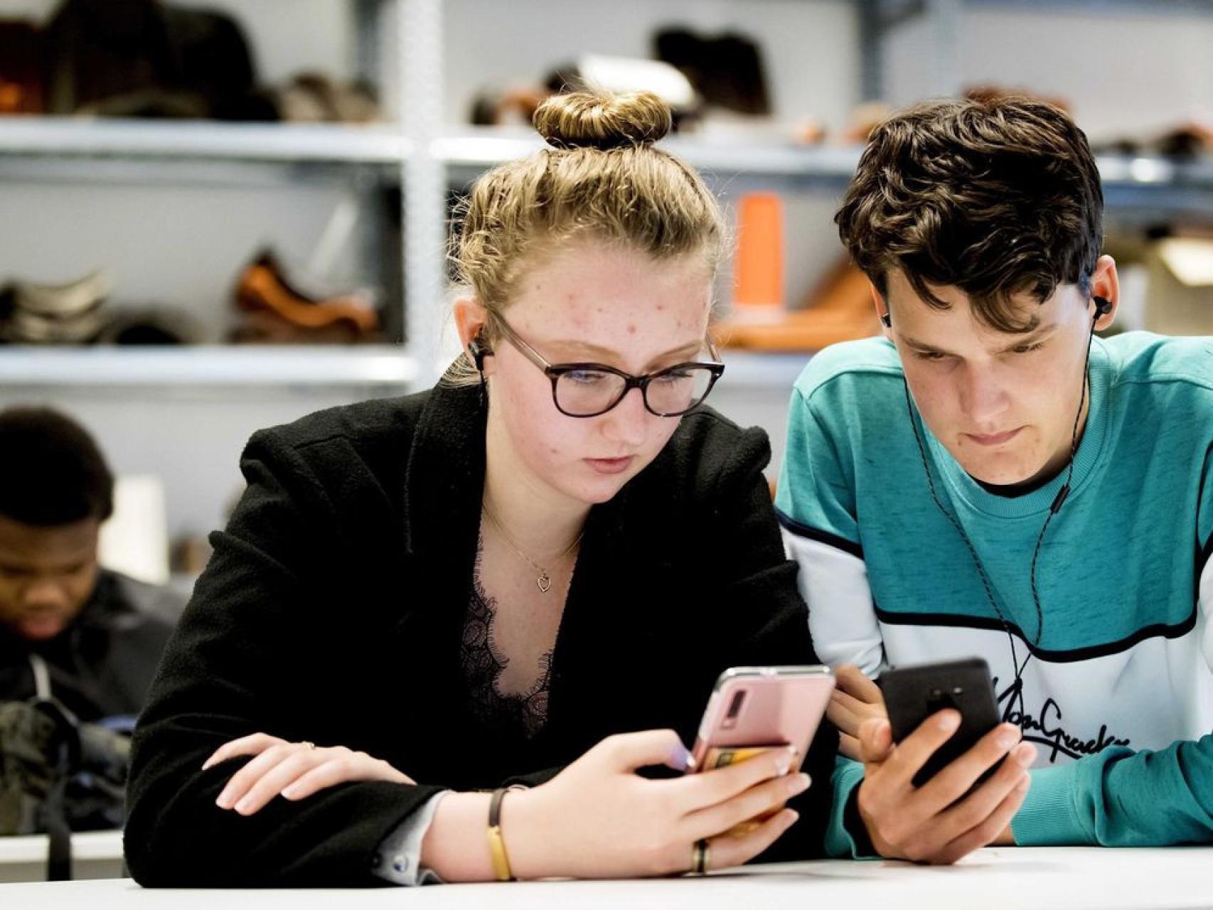 Dos adolescentes usan sus dispositivos en el aula.