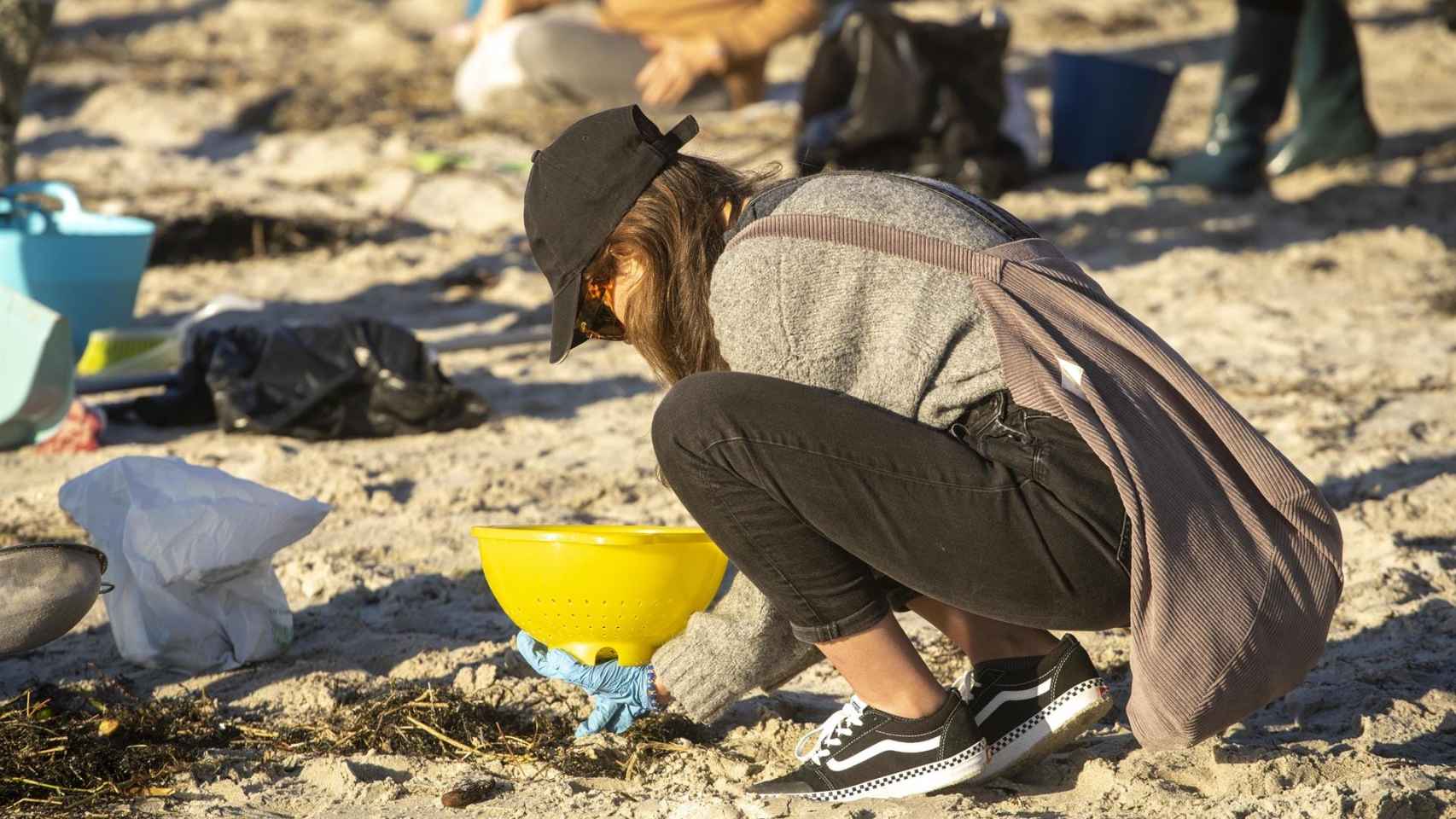 Varios voluntarios recogen pellets en la playa de Panxón, a 11 de enero de 2024.