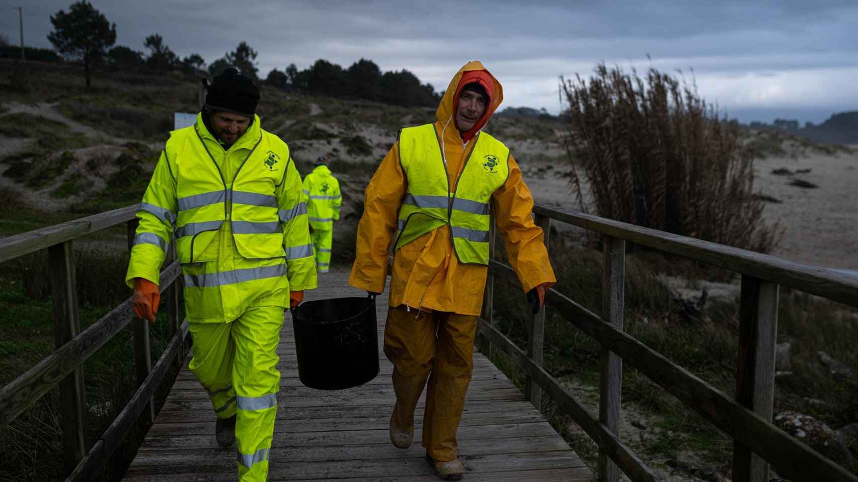 Dos hombres cargan un cubo lleno de pellets, en la playa Area Maior.