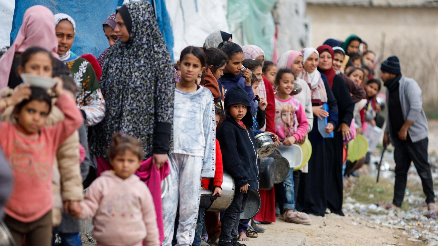 Mujeres y niñas palestinas hacen fila con cacerolas y platos para recibir comida, este miércoles en Rafah.