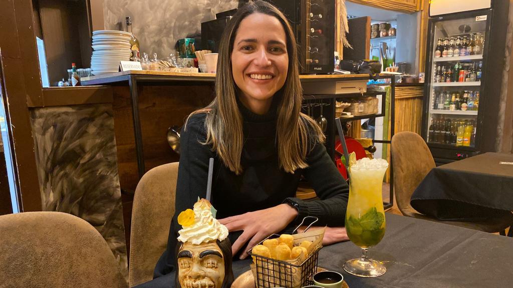 Abril Jiménez en la mesa de su restaurante con tequeños, piña colada (izq.) y mojito.