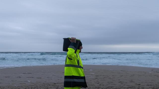 Un hombre carga un cubo lleno de pellets, en la playa Area Maior, en Muros, A Coruña