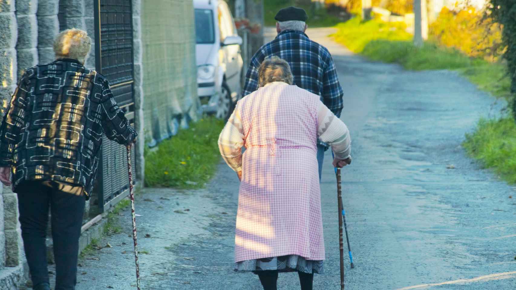 Tres personas mayores caminan por un pueblo.