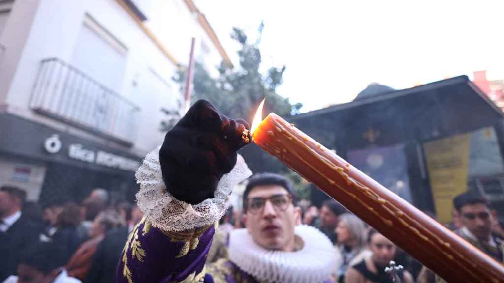 Un acolito del El cristo de los Javieres enciende un cirio al caer la tarde en Sevilla