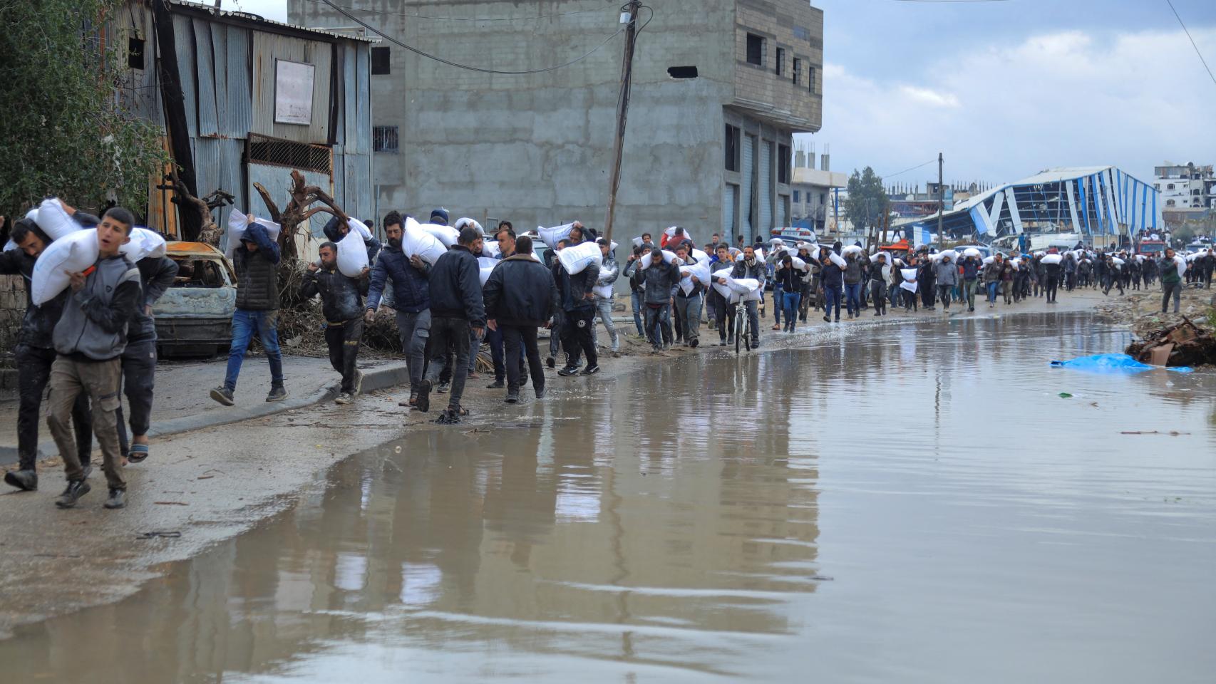 Palestinos transportan bolsas de harina que cogieron de un camión de ayuda cerca de un puesto de control israelí, en la ciudad de Gaza, el 27 de enero de 2024.