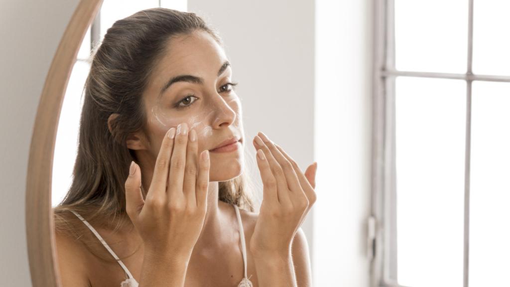 Una mujer aplicándose crema en el rostro.