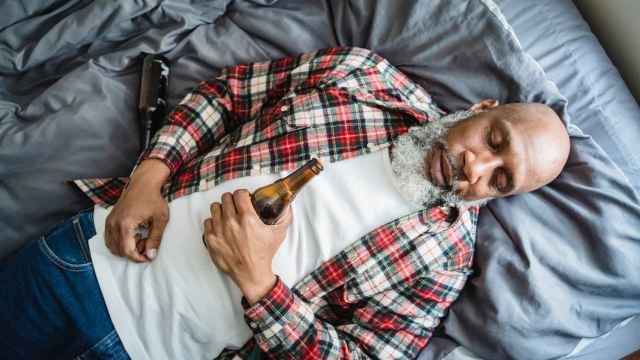 Imagen de archivo de una persona acostada con una cerveza en la cama.