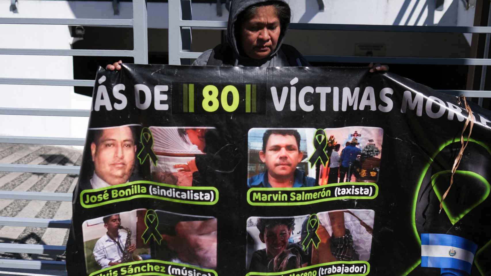 Una mujer sostiene un cartel con fotos de personas que murieron detenidas en una protesta ante la Fiscalía General de El Salvador.