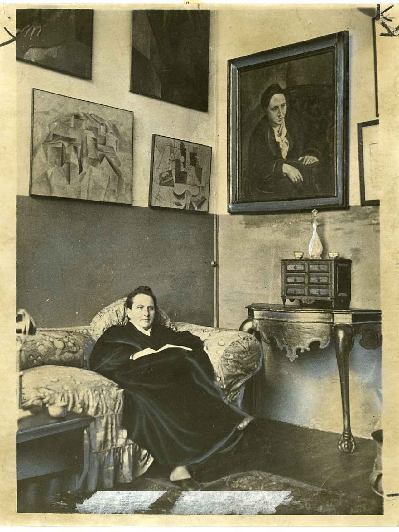 Gertrude Stein, sentada en su estudio de París, con el célebre retrato que le hizo Pablo Picasso y otras pinturas de arte moderno colgadas en la pared.