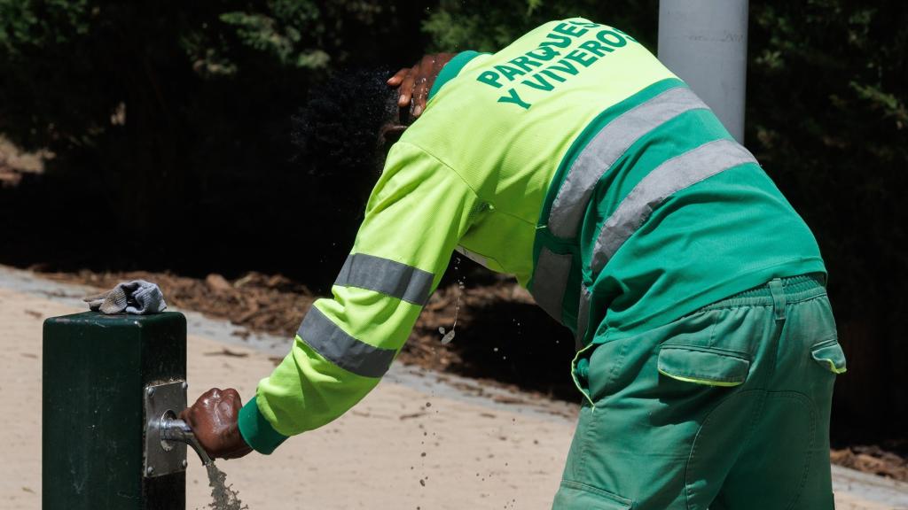 Un trabajador se refresca en una fuente.