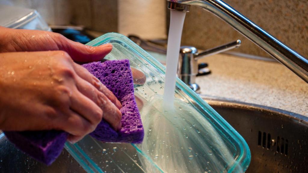Imagen de las manos de una persona lavando un táper.