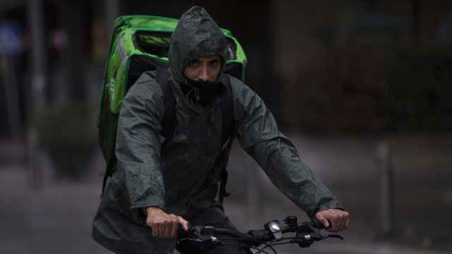 Un 'rider' (repartidor) trabaja bajo la lluvia protegido con un impermeable