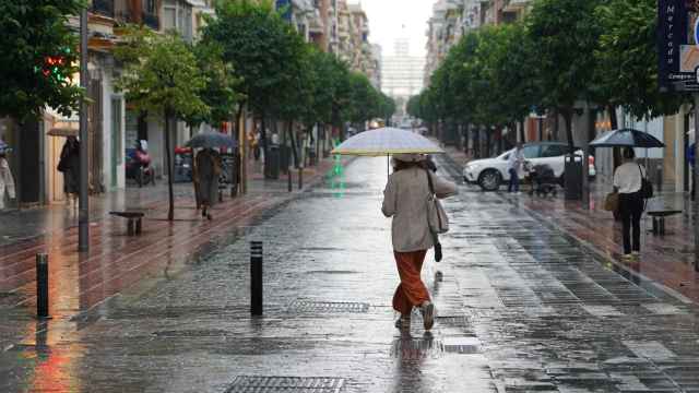 Sevillanos se protegen de la lluvia en la calle Asunción.