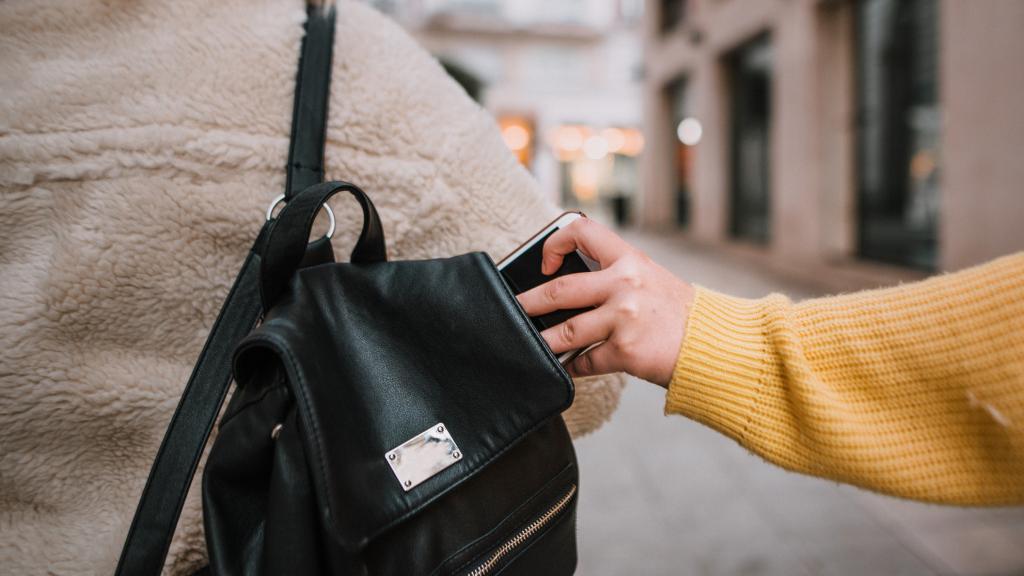 Una persona robando un móvil de un bolso.