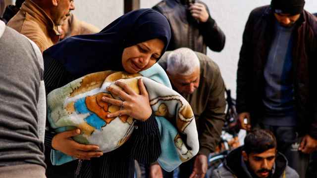 Una madre sostiene a su bebé mientras observa el cadáver de un ser querido, este jueves en Rafah.