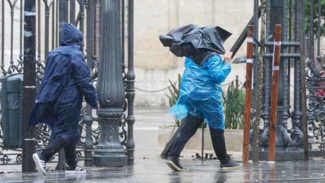 Dos personas tratan de protegerse en Sevilla de las lluvias de la borrasca Karlotta.
