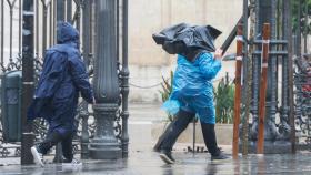 Dos personas tratan de protegerse en Sevilla de las lluvias de la borrasca Karlotta.