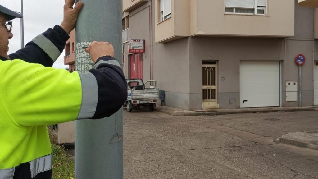 Un trabajador retira una pegatina de una farola.