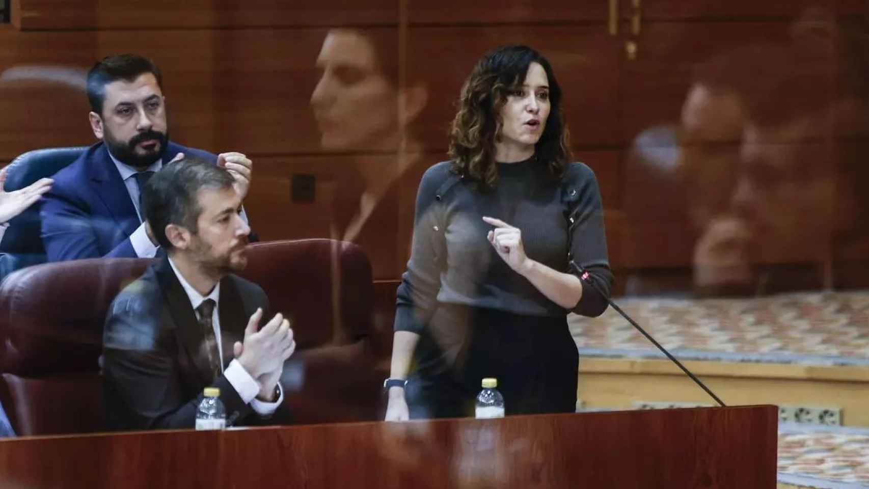 Isabel Díaz Ayuso en la Asamblea de Madrid con el reflejo de Monasterio en un cristal.