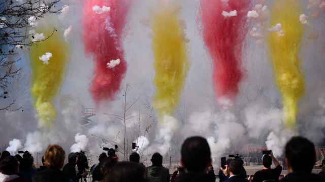 Varias personas observan el humo de colores durante la primera mascletá madrileña, en el Puente del Rey de Madrid.