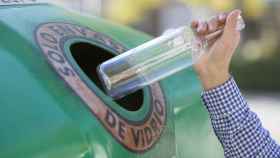 Imagen de una persona depositando una botella de vidrio al contenedor.
