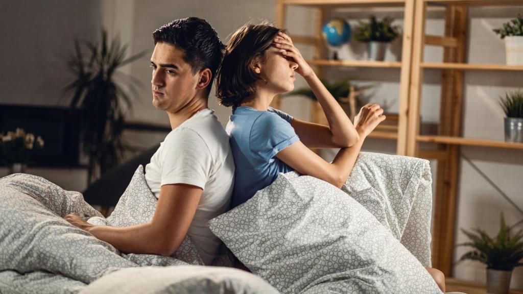 Pareja de espaldas sentados en la cama.