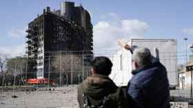 Dos personas contemplan el edificio de Valencia arrasado por las llamas.