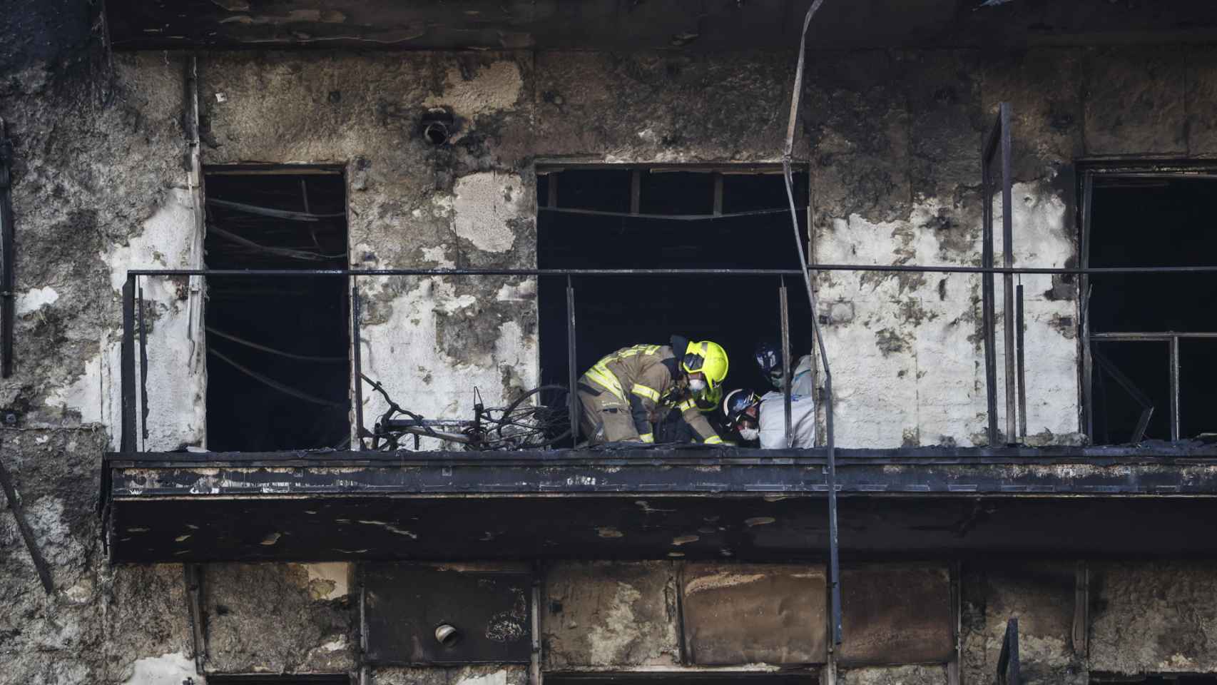 Bomberos y Policía Científica inspeccionan un cuerpo en un balcón del edificio incendiado.